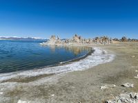 an empty beach is shown next to the water and snow - capped mountains on a sunny day