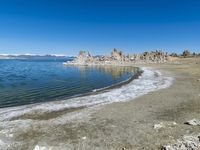 an empty beach is shown next to the water and snow - capped mountains on a sunny day