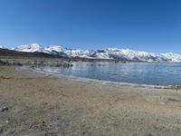an empty beach is shown next to the water and snow - capped mountains on a sunny day