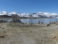 an empty beach is shown next to the water and snow - capped mountains on a sunny day