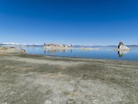 an empty beach is shown next to the water and snow - capped mountains on a sunny day
