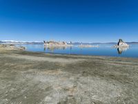 an empty beach is shown next to the water and snow - capped mountains on a sunny day