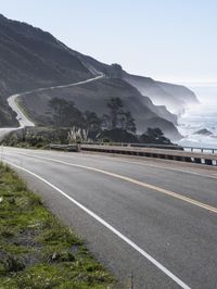 a curve in the road with trees and cliffs on both sides of it, along with the ocean on the opposite side