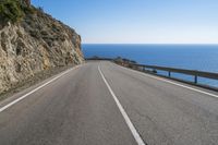 an empty road with a cliff side and ocean in the distance on the other side