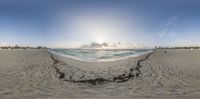 a fish eye lens with the beach and water in the back ground with sand in front of the camera