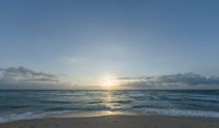 a sandy beach with waves lapping on it and the sun setting behind the horizon