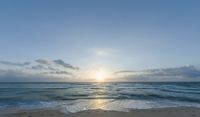 a sandy beach with waves lapping on it and the sun setting behind the horizon