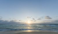 a sandy beach with waves lapping on it and the sun setting behind the horizon