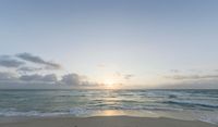 a sandy beach with waves lapping on it and the sun setting behind the horizon