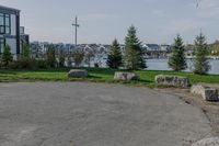 a park near the water with rocks on the road and houses on the other side