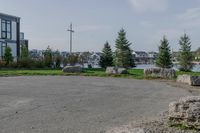 a park near the water with rocks on the road and houses on the other side