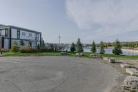 a park near the water with rocks on the road and houses on the other side