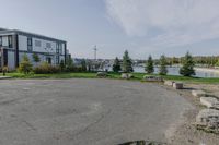 a park near the water with rocks on the road and houses on the other side