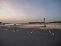 an empty parking lot sitting in front of a body of water at sunset with one person walking near water