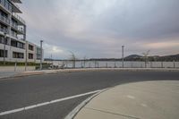 a parking lot that has buildings by the water on both sides of it, and a fence next to it