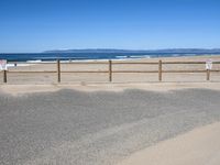 a paved beach with a fence in front of it and the ocean in the distance