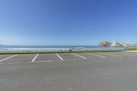 an empty parking lot with no cars in the parking lot near the ocean and cliffs in the background