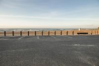 an empty parking lot near the ocean with sand on top of it and a surfboard that is standing up