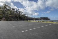 a parking lot near the ocean with some trees and rocks on the ground and in the distance, people