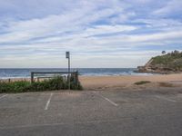 a bench in a parking lot next to the sea and a hill with ocean waves