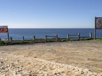 a brown sign on top of a dirt field next to the water and the sea