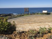 a picnic area with the ocean in the background next to a bench, surrounded by plants