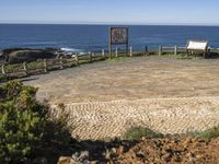 a picnic area with the ocean in the background next to a bench, surrounded by plants