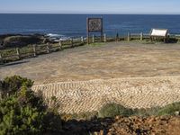 a picnic area with the ocean in the background next to a bench, surrounded by plants