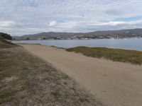 a path leads to the beach with green grass and a body of water in the distance