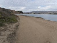 a path leads to the beach with green grass and a body of water in the distance