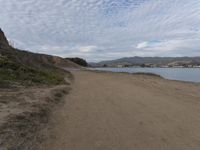 a path leads to the beach with green grass and a body of water in the distance