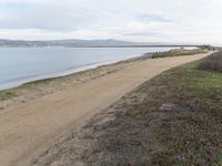 a path leads to the beach with green grass and a body of water in the distance