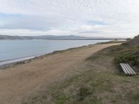 a path leads to the beach with green grass and a body of water in the distance