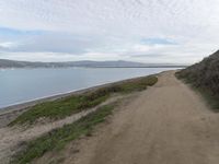 a path leads to the beach with green grass and a body of water in the distance