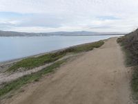 a path leads to the beach with green grass and a body of water in the distance