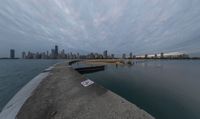 a cloudy view shows the water below a pier on lakefront with buildings in the distance