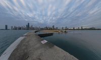 a cloudy view shows the water below a pier on lakefront with buildings in the distance