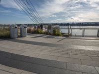 a brick walkway on the other side of the water and a rail with several trash cans