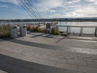 a brick walkway on the other side of the water and a rail with several trash cans