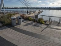 a brick walkway on the other side of the water and a rail with several trash cans