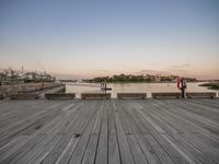 a long wooden boardwalk with benches next to it at sunset with a body of water