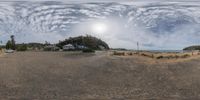 an empty sandy lot near a beach and ocean, and a sky full of clouds