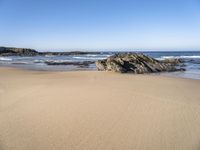 the sand and blue ocean are very calm on this beach as the water comes up from the rocks