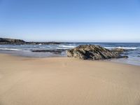 the sand and blue ocean are very calm on this beach as the water comes up from the rocks