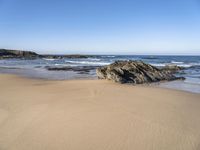 the sand and blue ocean are very calm on this beach as the water comes up from the rocks