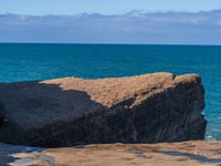 a person stands on rocks in the water while the ocean looks out to the horizon