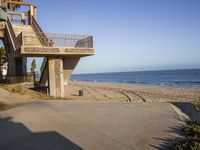 a concrete building on the beach near the ocean with a staircase going up it and a bench at the bottom