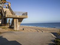 a concrete building on the beach near the ocean with a staircase going up it and a bench at the bottom