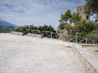 a wooden fence and concrete walls with trees in the background and water below it to the side