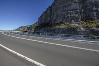 a car is driving along a curving road near mountains and a cliff at the background